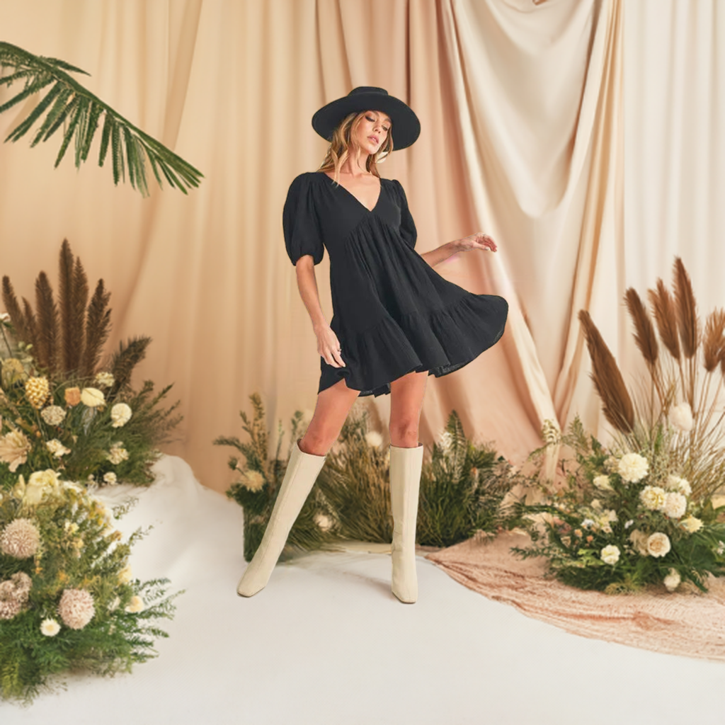 This short sleeve black mini dress features a charming tied back detail and playful ruffled accents.